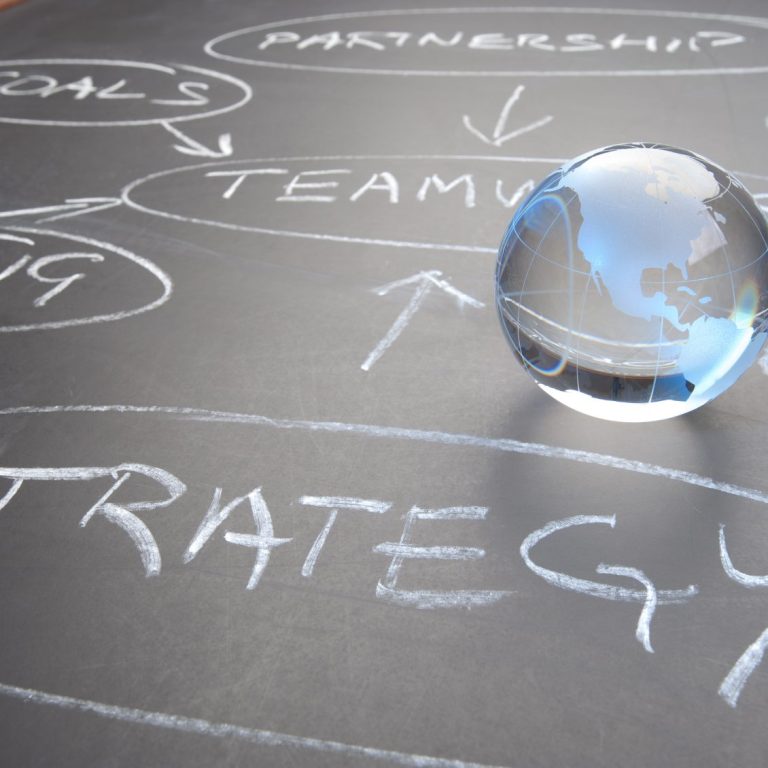 Glass marble world globe on a blackboard with strategic terms and arrows.