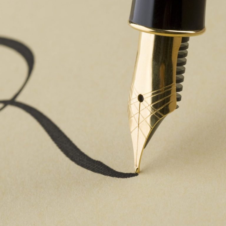 Close-up of a fountain pen making an unspecified cursive letter on cream-coloured paper.